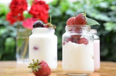 Sağlıklı kahvaltı - ev yapımı puding veya yoğurt taneciği, çilek, kiraz, hanımeli böğürtlen, fındık ve yoğurt. Vejetaryen konsept yiyecekler. Yeşil yaprakların arka planında puding ya da kokteyl.