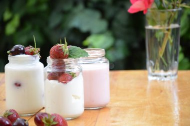 Sağlıklı kahvaltı - ev yapımı puding veya yoğurt taneciği, çilek, kiraz, hanımeli böğürtlen, fındık ve yoğurt. Vejetaryen konsept yiyecekler. Yeşil yaprakların arka planında puding ya da kokteyl.