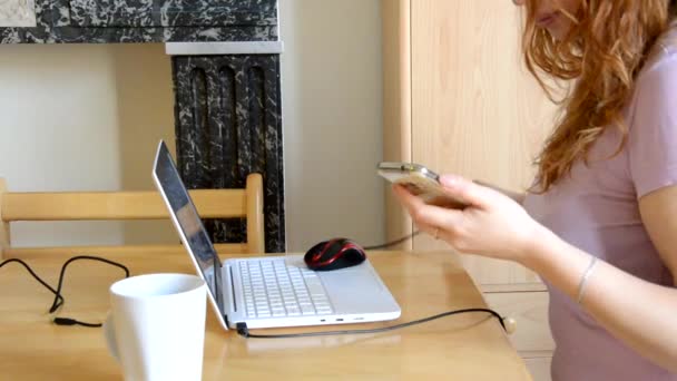 Vážná mladá žena na volné noze pracuje na volné noze z domova psaní e-mail na notebooku, dívka používající počítač pro studium on-line používá telefon, pije kávu nebo čaj, žena uživatel zaneprázdněn na dálku práci na internetu — Stock video
