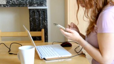 Karantina ve kendini izole etme sürecinde evden çalışan ciddi genç kadın dizüstü bilgisayarda e-posta yazıyor, internetten telefon kullanıyor, kahve ya da çay içiyor, internet üzerinden çalışan bir kadın.