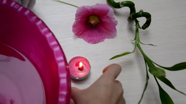 Hintergrund eines Thermalbades mit rosa Blume, weißem Handtuch zusammengerollt und einem Zweig grünen Bambusmädchens, das eine Kerze entzündet — Stockvideo