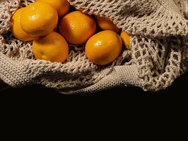 Tangerines in a knitted bag. Isolated black background