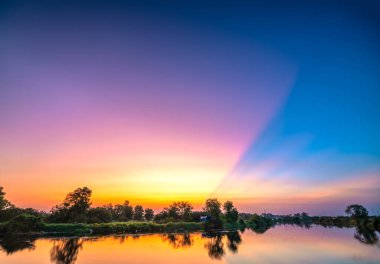 Ufukta güneş çarpıcı bir şekilde parlıyor bulutlar arasında, nehir kenarında sihirli mor gün batımı.