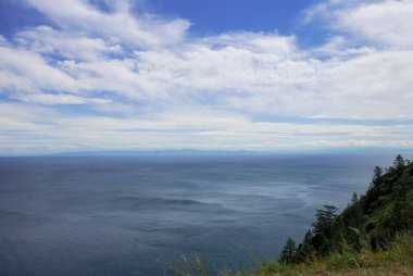 Mavi Gökyüzü bulutlu deniz yüzeyi üzerinde. Güneşli bir gün görünümünde kayalık sahil