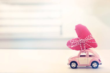 Kalp yastık taşıyan minyatür pembe araba 