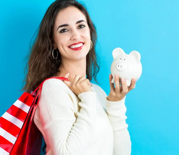 Mulher segurando banco porquinho e sacos de compras — Fotografia de Stock