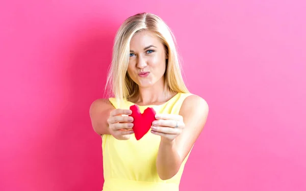 Happy young woman holding a heart cushion — Stock Photo, Image