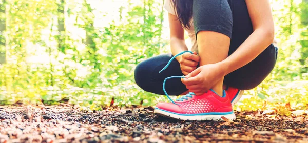 Kvinnliga joggaren knyta sina skor i skogen — Stockfoto