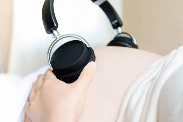 Giovane donna incinta con le cuffie sulla pancia — Foto Stock