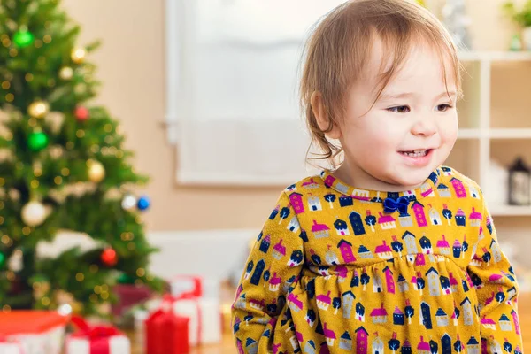 Kleuter meisje glimlachend tegenover een kerstboom — Stockfoto