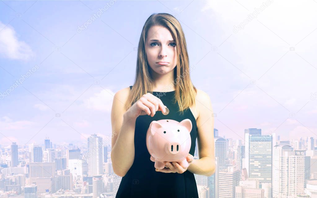 Unhappy young woman with pink piggy bank