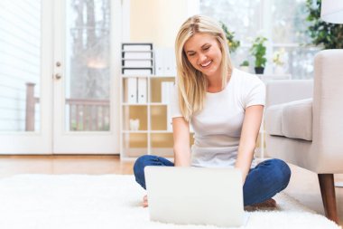 Evde dizüstü bilgisayar kullanan genç bir kadın.