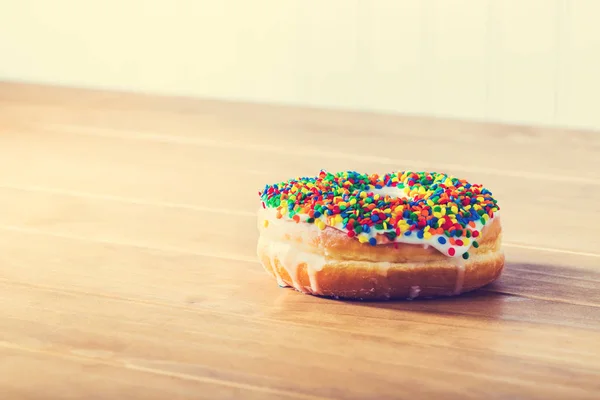 Sprinkled donut on a wooden table — Stock Photo, Image