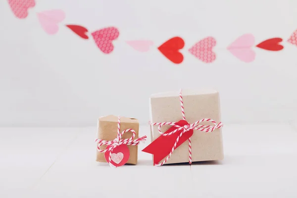 Pequenas caixas de presente com corações pendurados acima — Fotografia de Stock