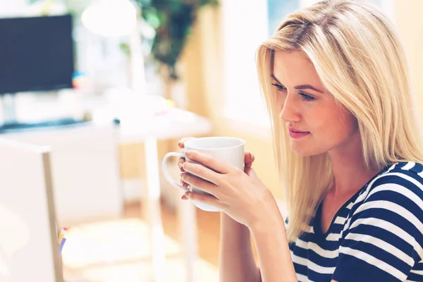 Jonge vrouw drinken koffie in een kantoor — Stockfoto