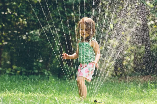Glada barn girl spelar i en sprinkler — Stockfoto