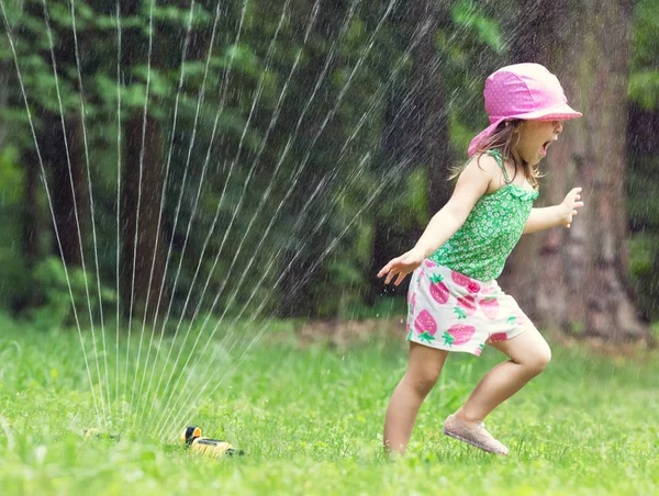 スプリンクラーで遊ぶ幼児の女の子 — ストック写真