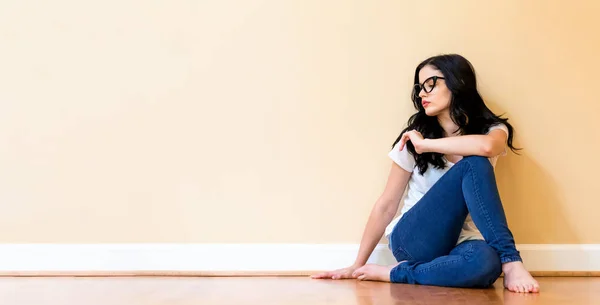 Молодая женщина в очках сидит на полу — стоковое фото