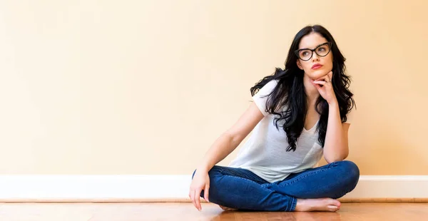 Jonge vrouw met glazen zittend op de vloer — Stockfoto