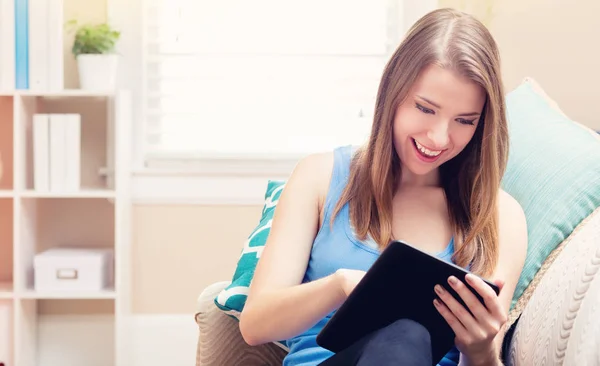 Glad ung kvinna läser en e-bok på hennes soffa — Stockfoto