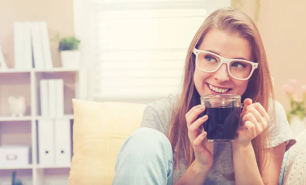 Glückliche junge Frau trinkt Kaffee auf ihrer Couch — Stockfoto