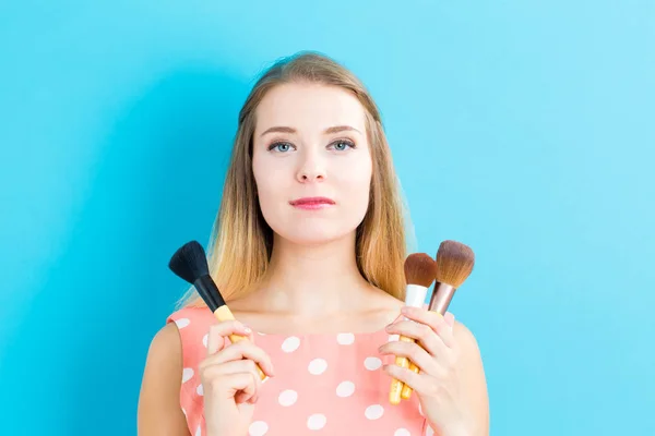 Hermosa mujer joven sosteniendo cepillos de maquillaje — Foto de Stock