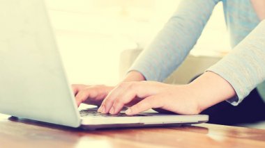 Parlak bir odada bir dizüstü bilgisayar üzerinde çalışan kadın