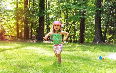 Bir yağmurlama oynarken mutlu yürümeye başlayan çocuk kız