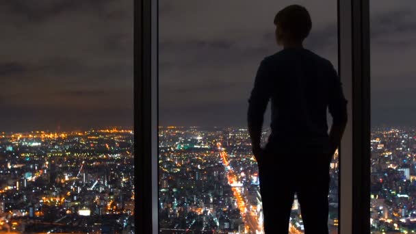 Mann blickt aus einem Fenster hoch über der Stadt — Stockvideo