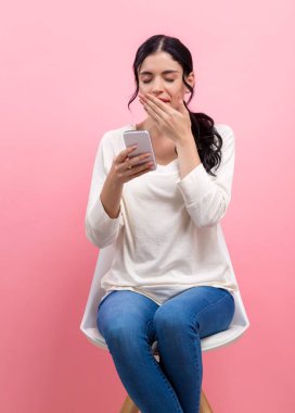 Akıllı telefonu olan genç bir kadın bir şeyler düşünüyor.