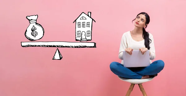 Casa e dinheiro na escala com a mulher usando um laptop — Fotografia de Stock