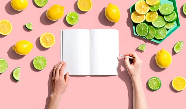 Person writing in notebook with lemons and limes — Stok fotoğraf