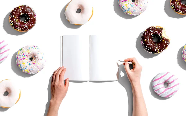 Person writing in a notebook with donuts — Stockfoto