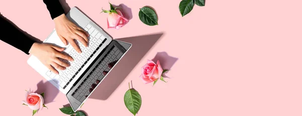 Kvinna som använder sin bärbara dator med rosa rosor — Stockfoto