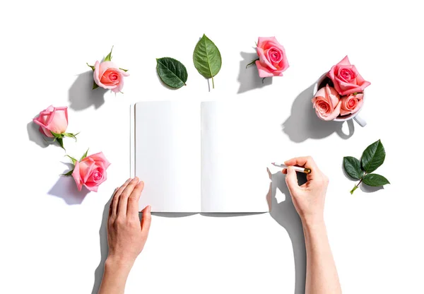 Mulher escrevendo em um caderno com rosas rosa — Fotografia de Stock