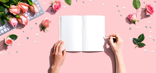 Mulher escrevendo em um caderno com rosas rosa — Fotografia de Stock