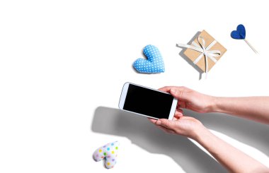 Akıllı telefonunu küçük bir hediye ve kalp minderiyle tutan bir kadın.