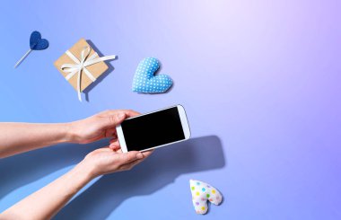 Akıllı telefonunu küçük bir hediye ve kalp minderiyle tutan bir kadın.