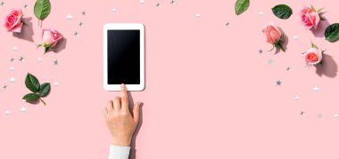 Tablet bilgisayarını pembe güllü bir kadın kullanıyor.