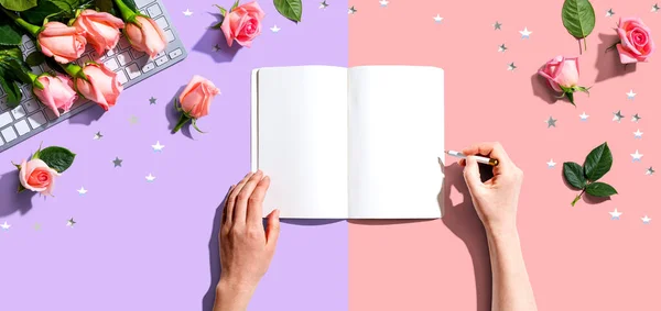 Mulher escrevendo em um caderno com rosas rosa — Fotografia de Stock