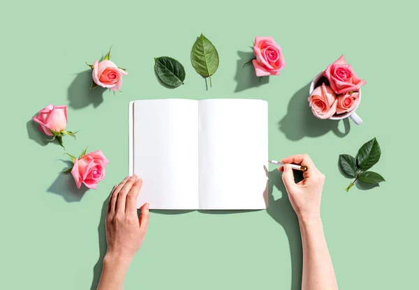 Femme écrivant dans un carnet avec des roses roses — Photo