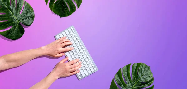 Persona usando un teclado de computadora con hojas tropicales — Foto de Stock