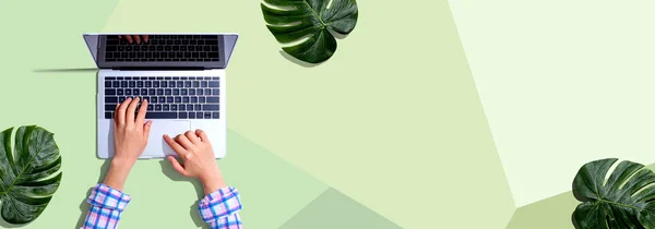 Pessoa que utiliza um computador portátil com folhas tropicais — Fotografia de Stock