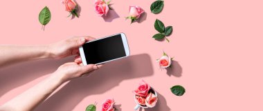Akıllı telefonunu pembe güllerle tutan bir kadın.