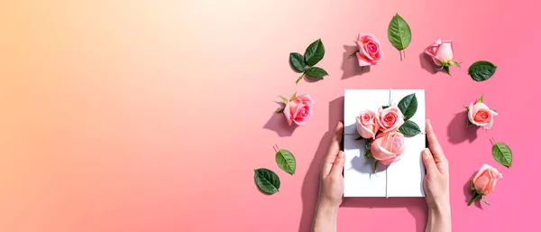 Manos femeninas sosteniendo una caja de regalo con rosas rosadas — Foto de Stock