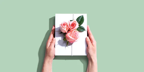 Manos femeninas sosteniendo una caja de regalo con rosas rosadas —  Fotos de Stock