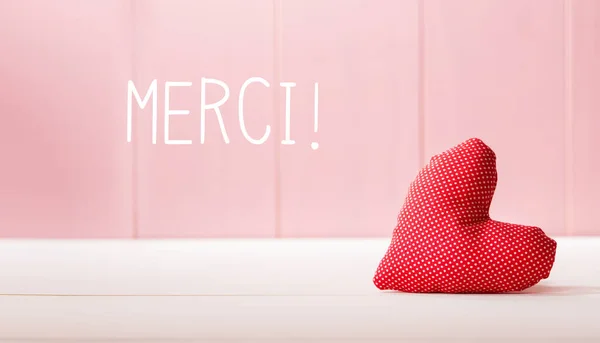 Merci - Gracias en francés con un cojín de corazón rojo —  Fotos de Stock