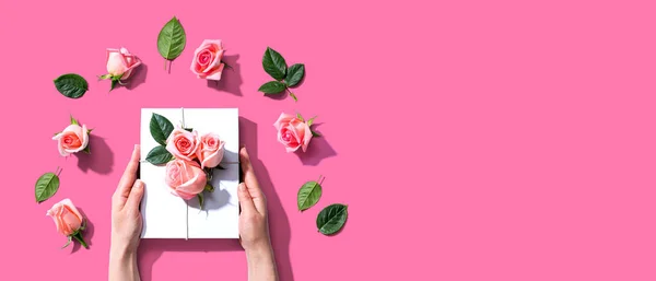 Manos femeninas sosteniendo una caja de regalo con rosas rosadas — Foto de Stock