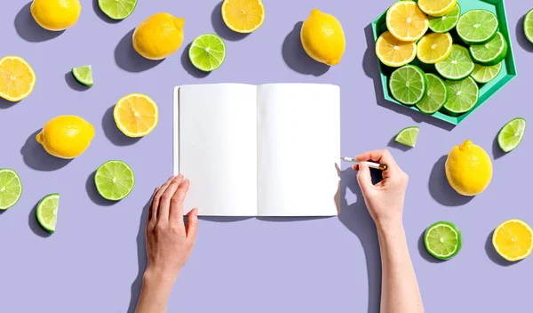 Person writing in notebook with lemons and limes — ストック写真