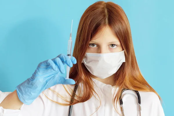 A teen girl plays doctor, a concept of choosing a profession for a child, a red hair girl in a white shirt, wearing a protective face mask and with a phonendoscope in her hands